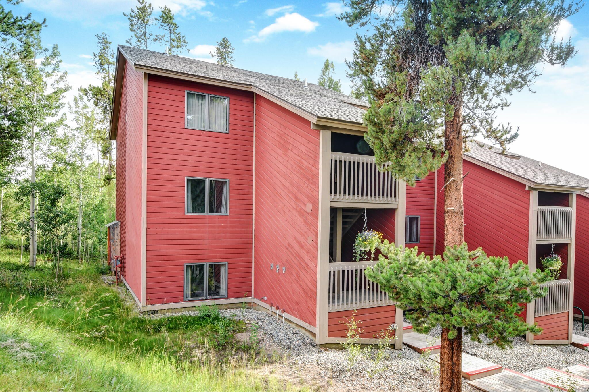 A red building with multiple windows and balconies, surrounded by trees and gravel.