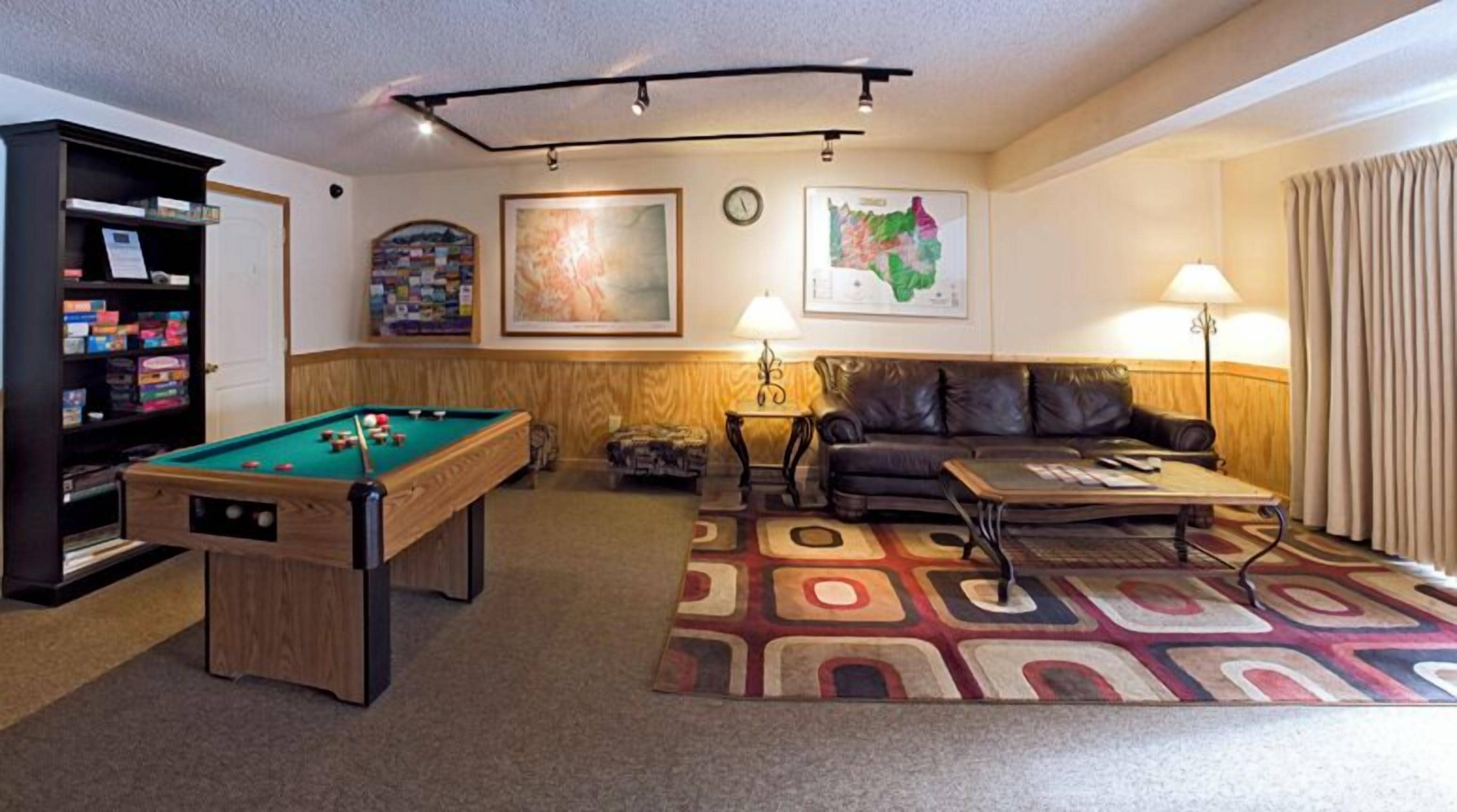 A pool table, a sofa, a lamp, and a bookshelf in a room with a patterned carpet.