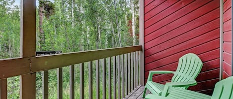 A wooden deck with a red wall and a view of trees. There are two green chairs on the deck.