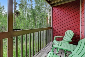 Une terrasse en bois avec un mur rouge et une vue sur les arbres. On y trouve deux chaises vertes.