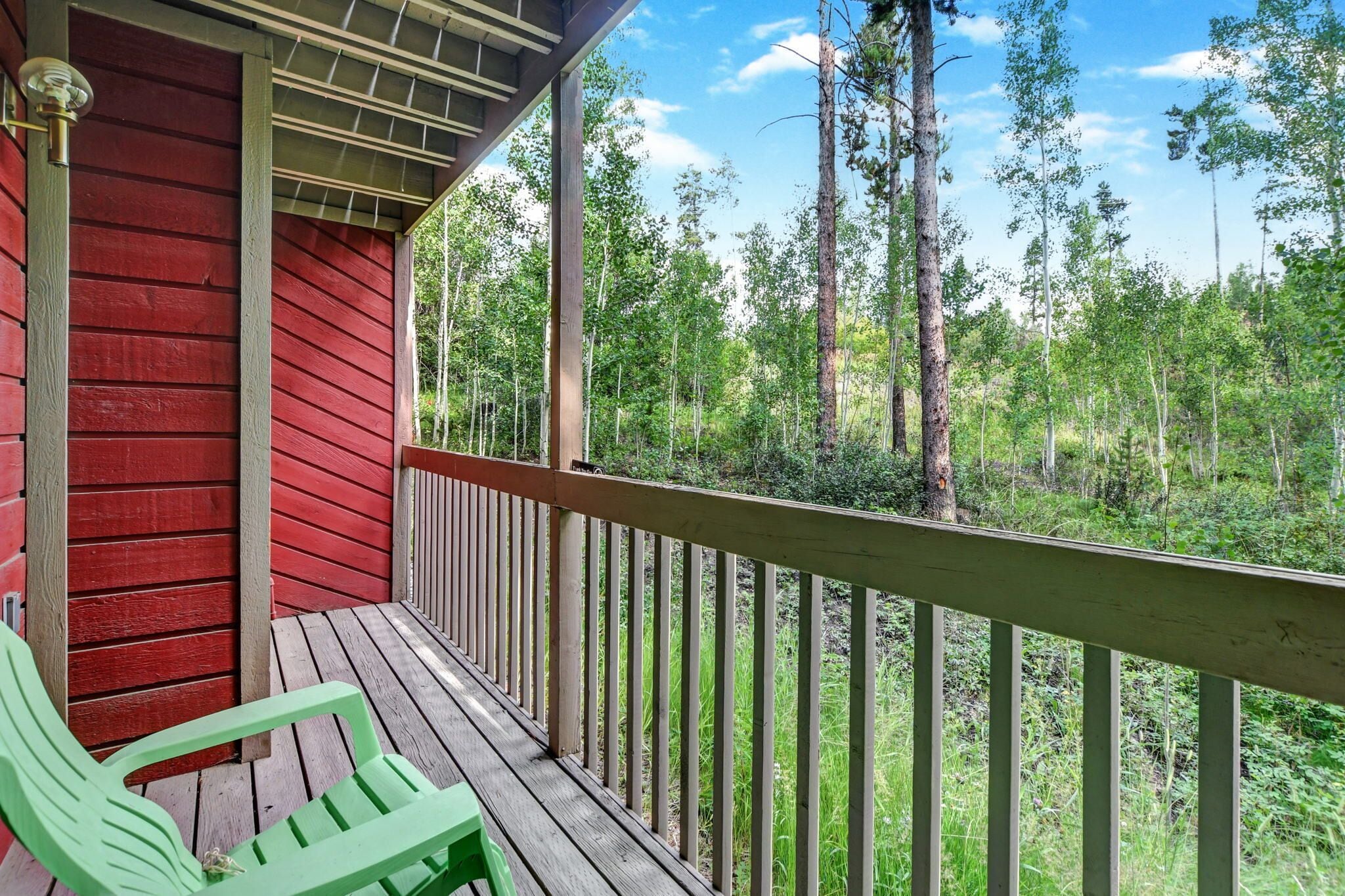 A wooden deck with a red wall and a railing overlooking a forested area.