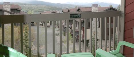 A balcony with green chairs and a table, overlooking a mountainous landscape.