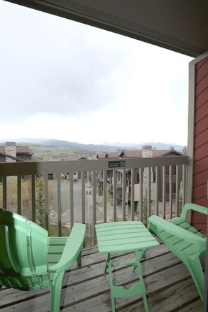 Un balcon avec des chaises vertes et une table, d’où l’on peut admirer un paysage montagneux.