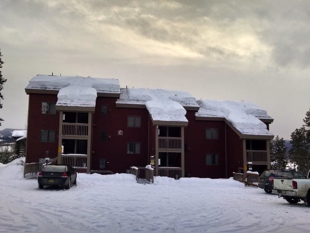 A multi-story building with snow-covered roofs and a parking area with several vehicles.