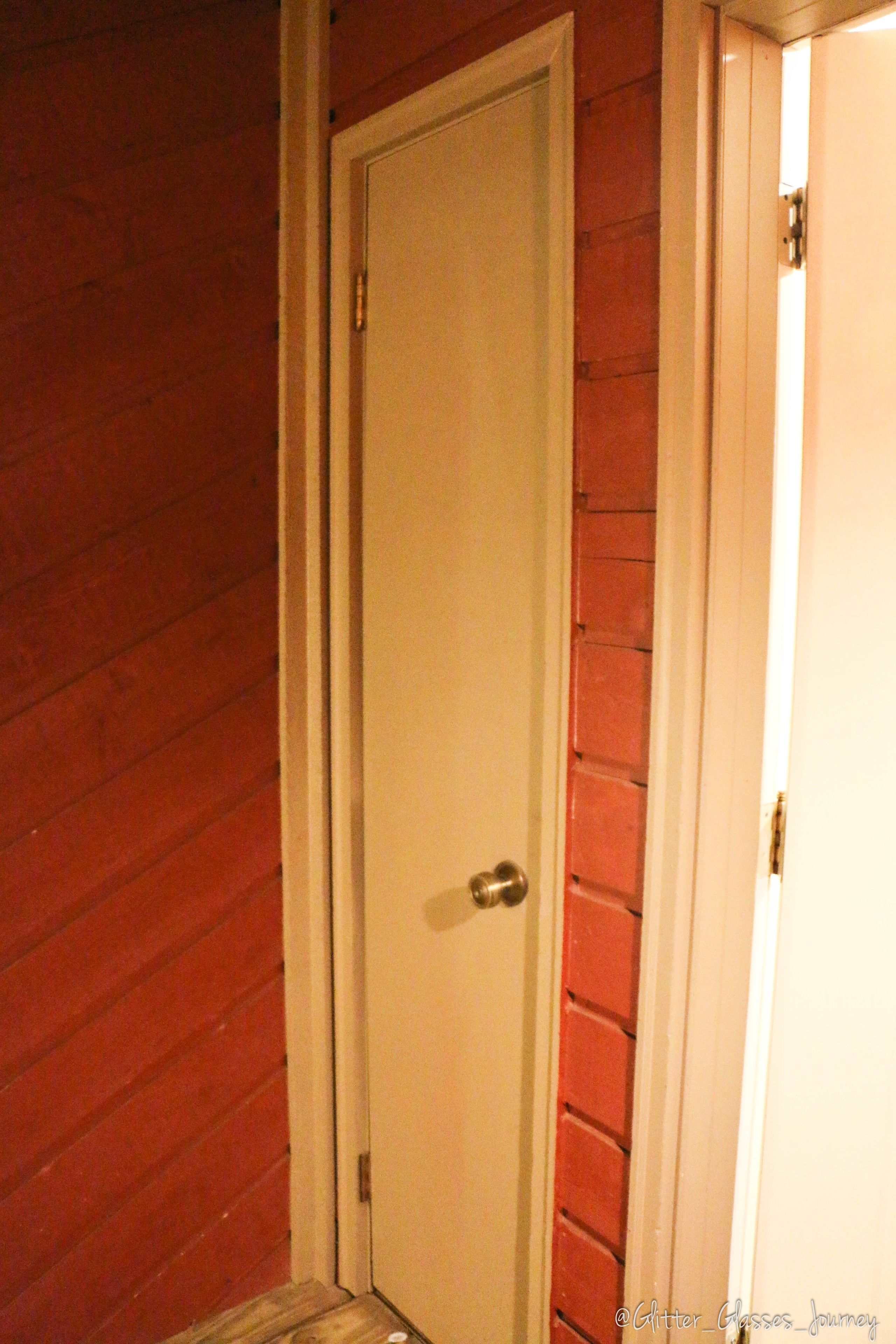 Una puerta blanca cerrada con un pomo plateado, integrada en una pared de madera con acabado rojo.