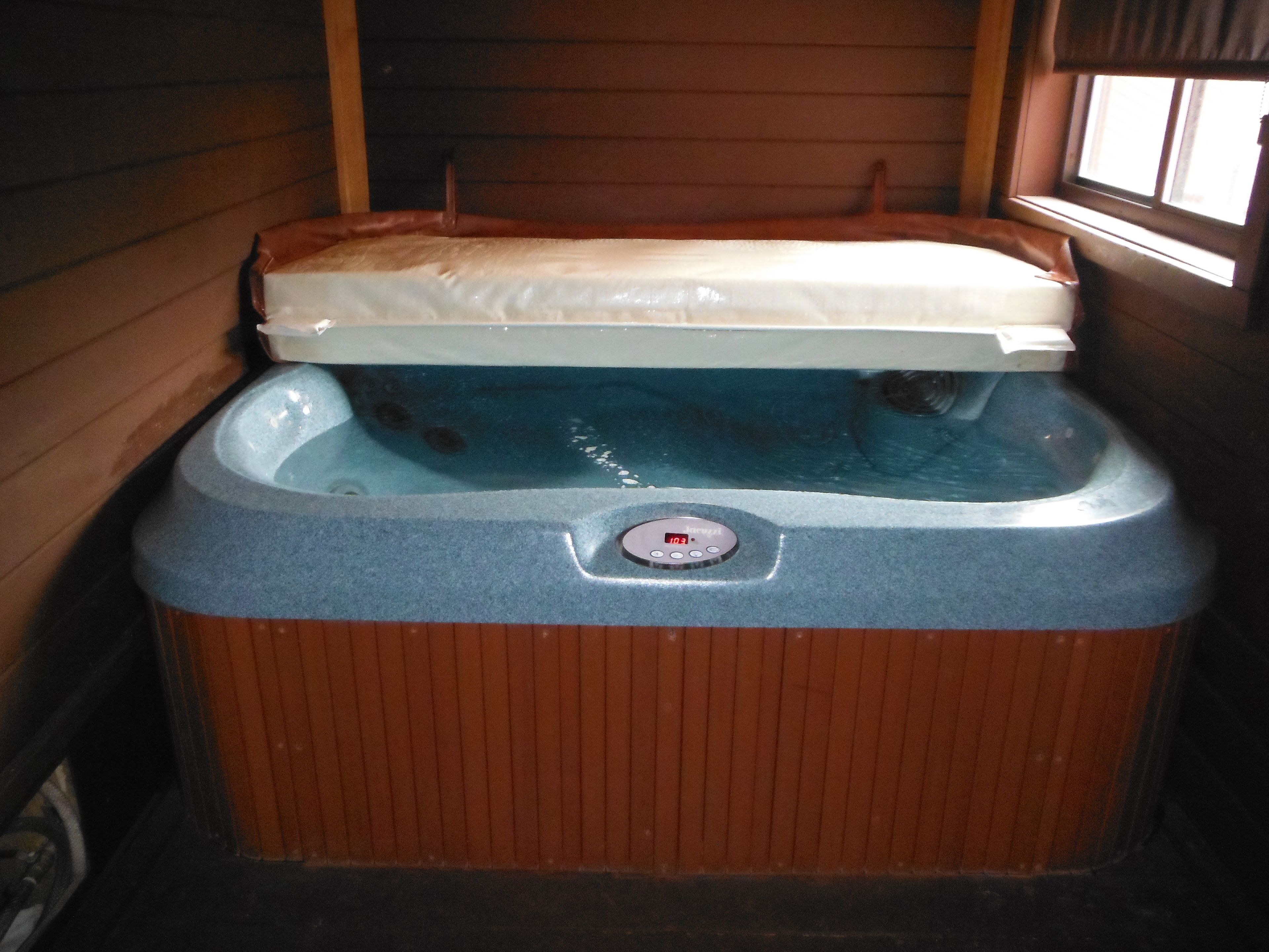 A hot tub with a digital control panel, wooden walls, and a window.