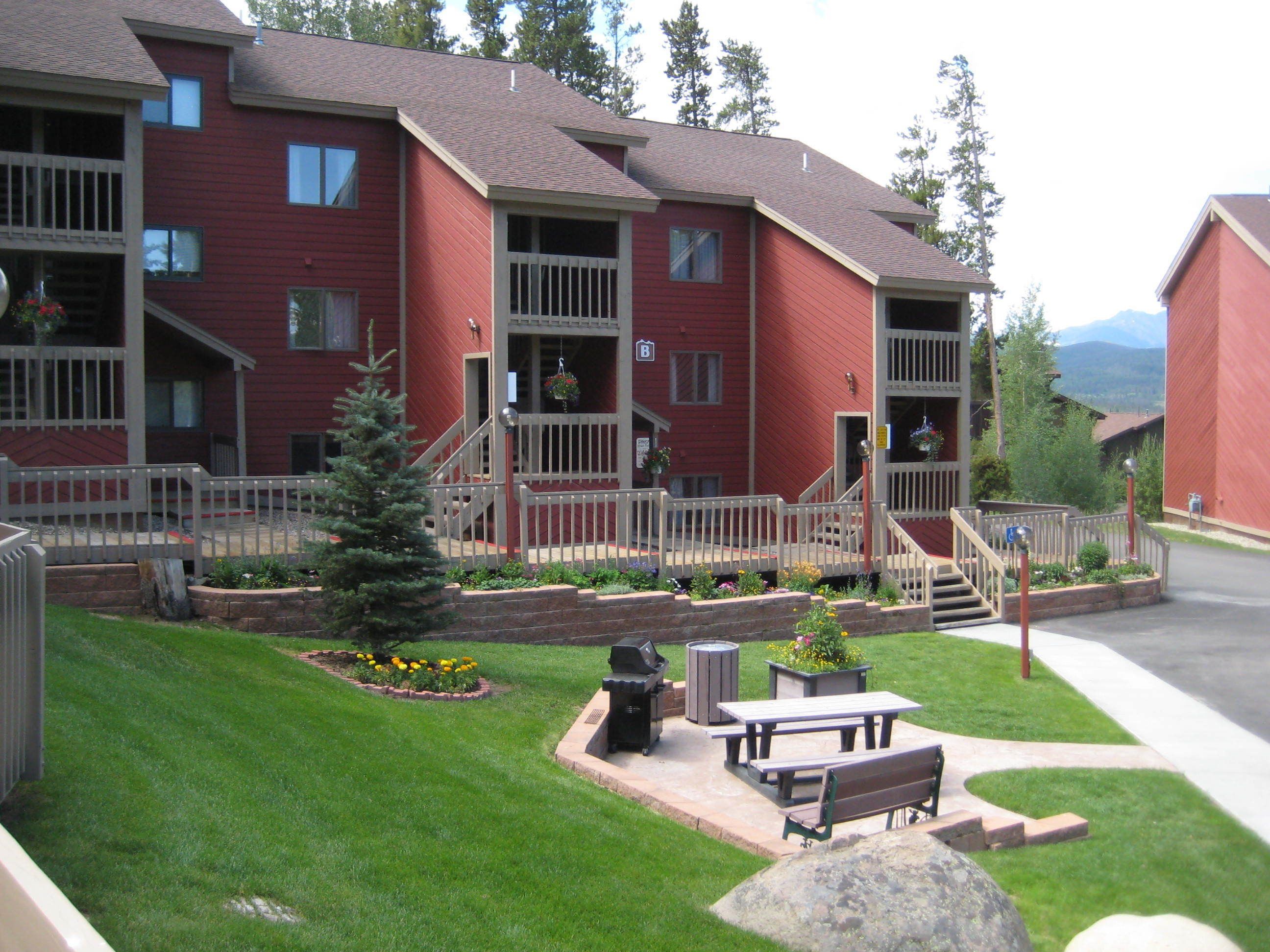 A red multi-story building with a front porch, outdoor seating, and a small tree.