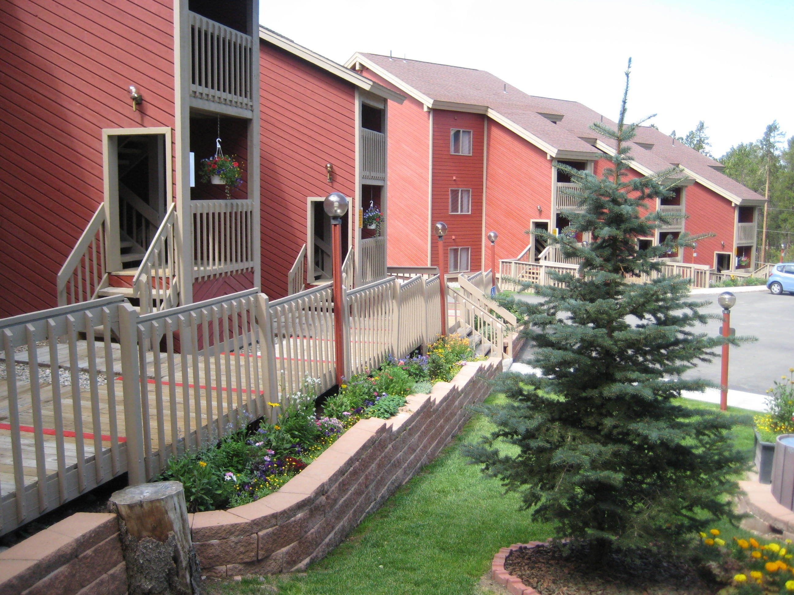 A red building with a white fence, a small tree, and a flower bed.