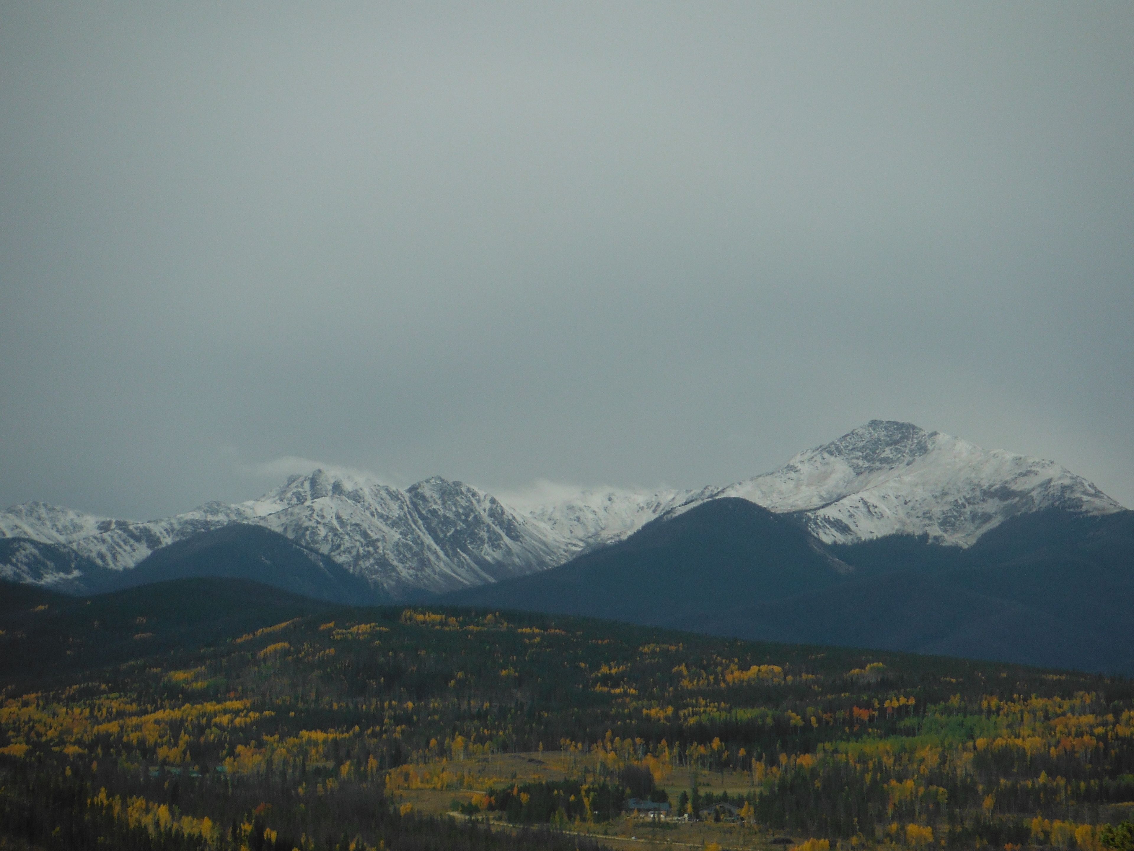 A mountainous landscape with snow-capped peaks and a forested valley below.