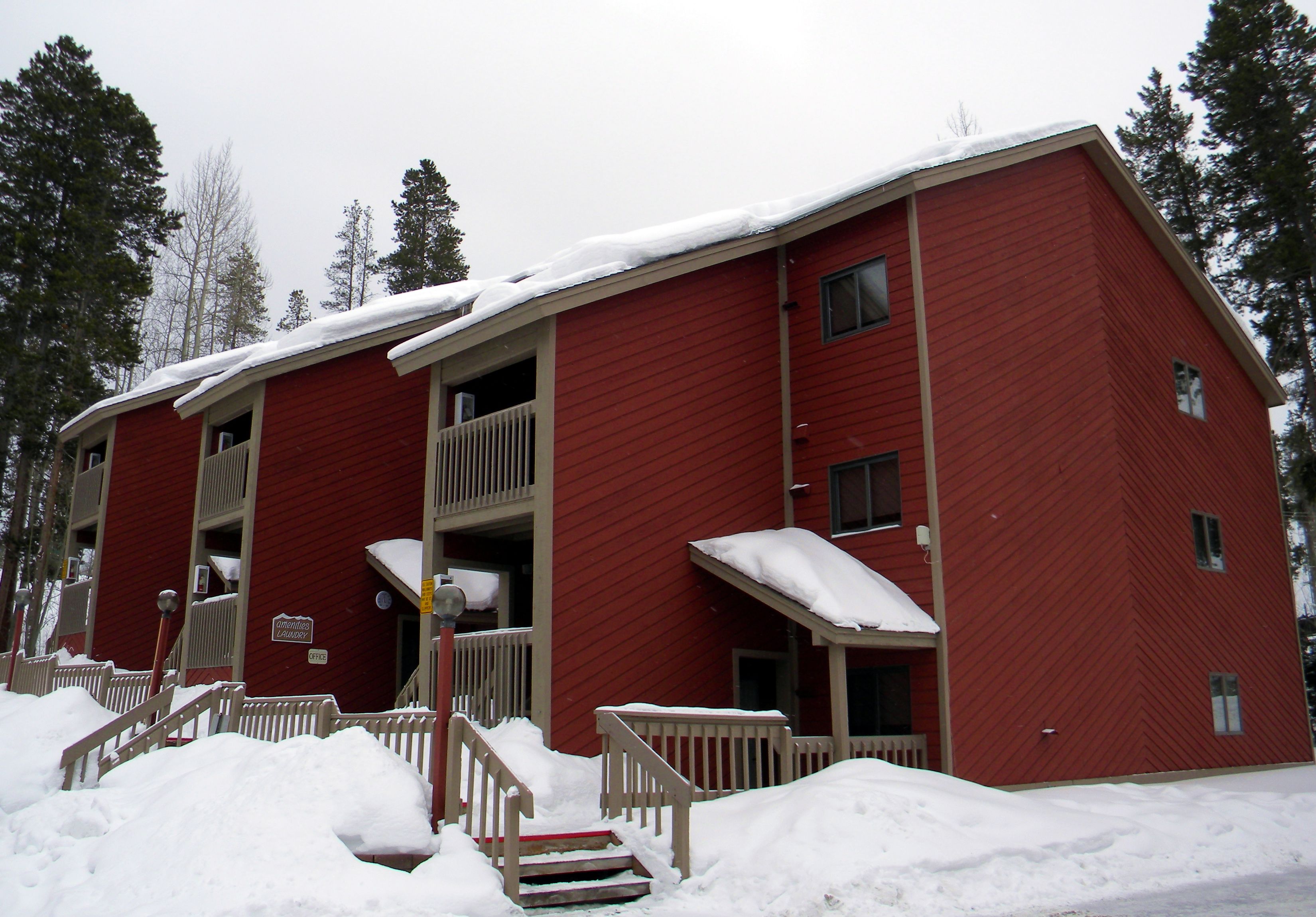 A red multi-story building with a balcony, surrounded by snow.