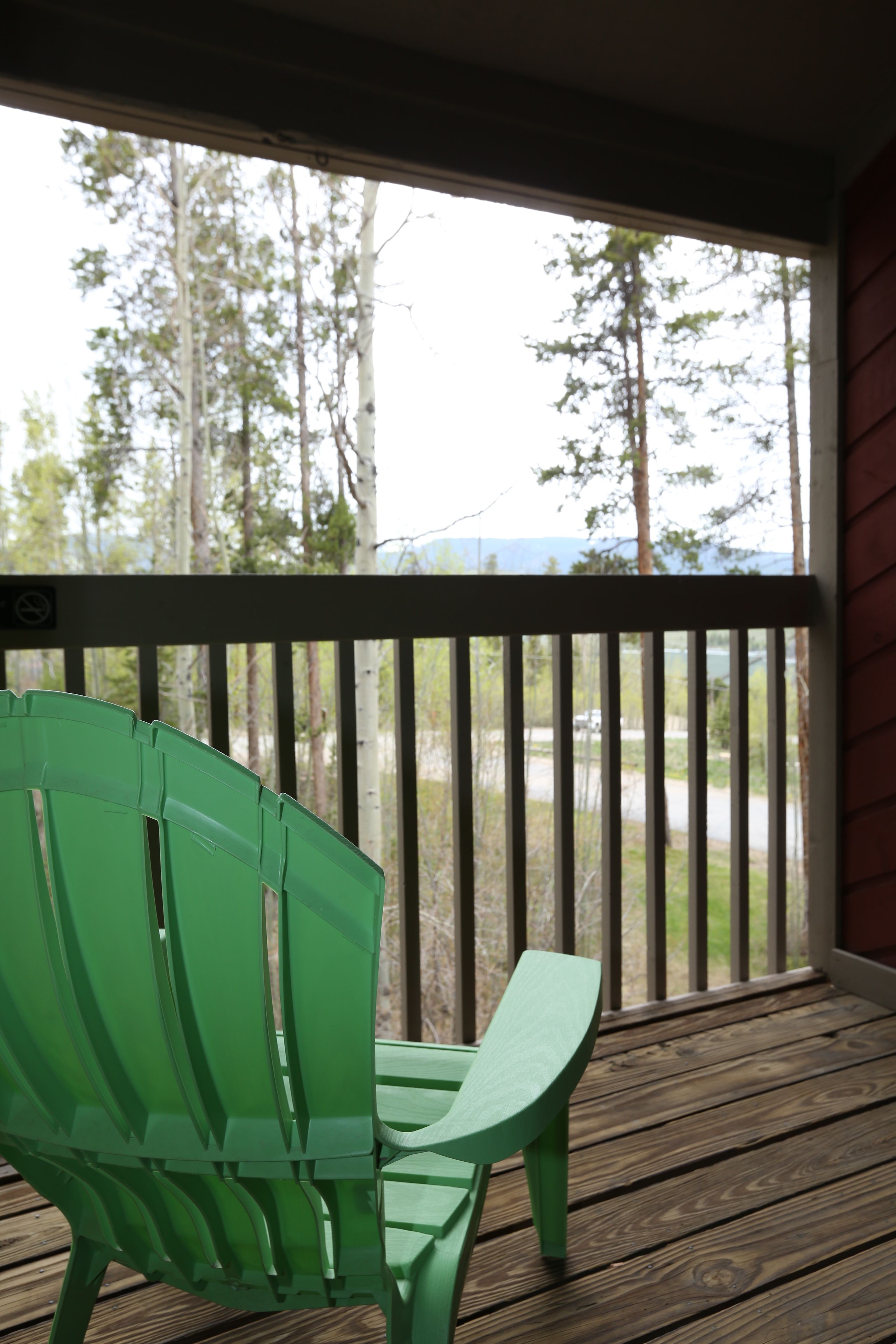 Une chaise verte sur une terrasse en bois dotée d’une rambarde, d’où l’on peut admirer une zone boisée et une étendue d’eau.