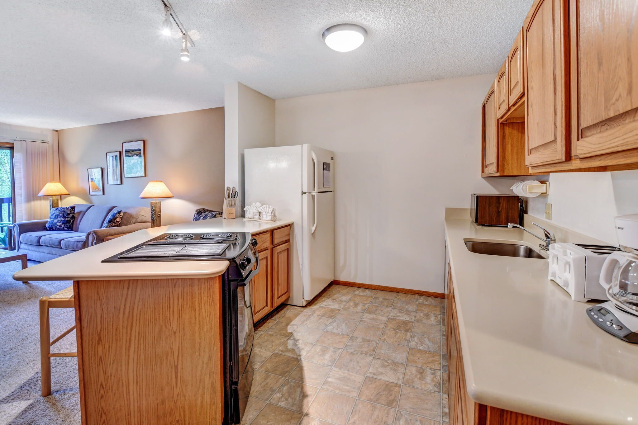 A compact kitchen with a central island, wooden cabinets, a refrigerator, and a toaster.