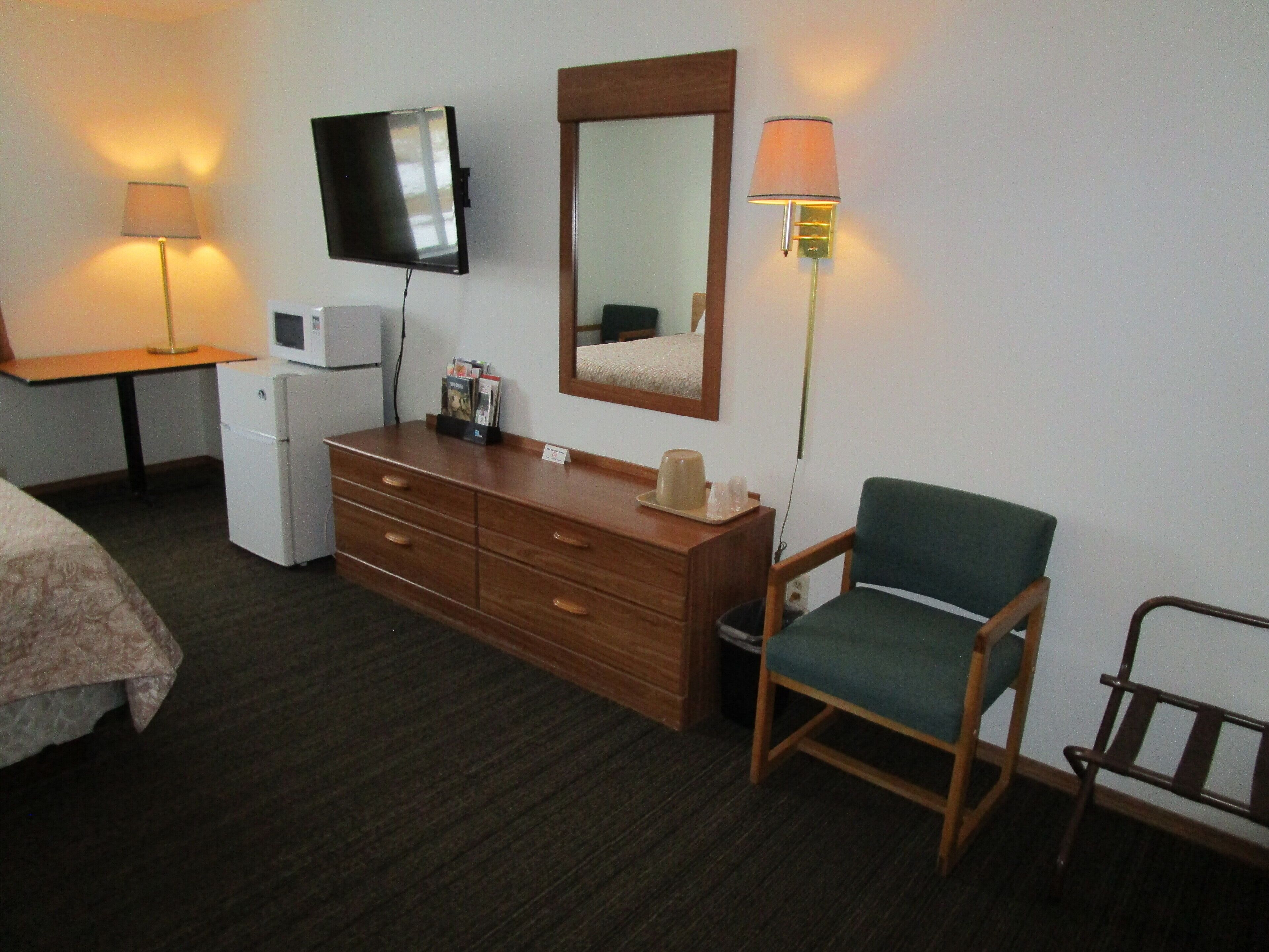 Une chambre d’hôtel comprenant un lit, une commode en bois, un bureau avec une lampe, une télévision et une chaise.