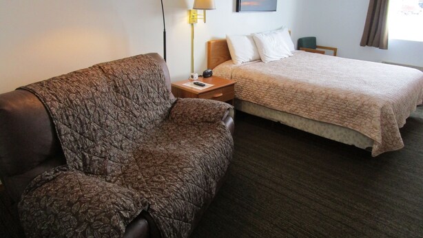Une chambre d’hôtel avec un canapé, un lit, une table de chevet, une lampe, un tableau au mur et une fenêtre avec des rideaux.