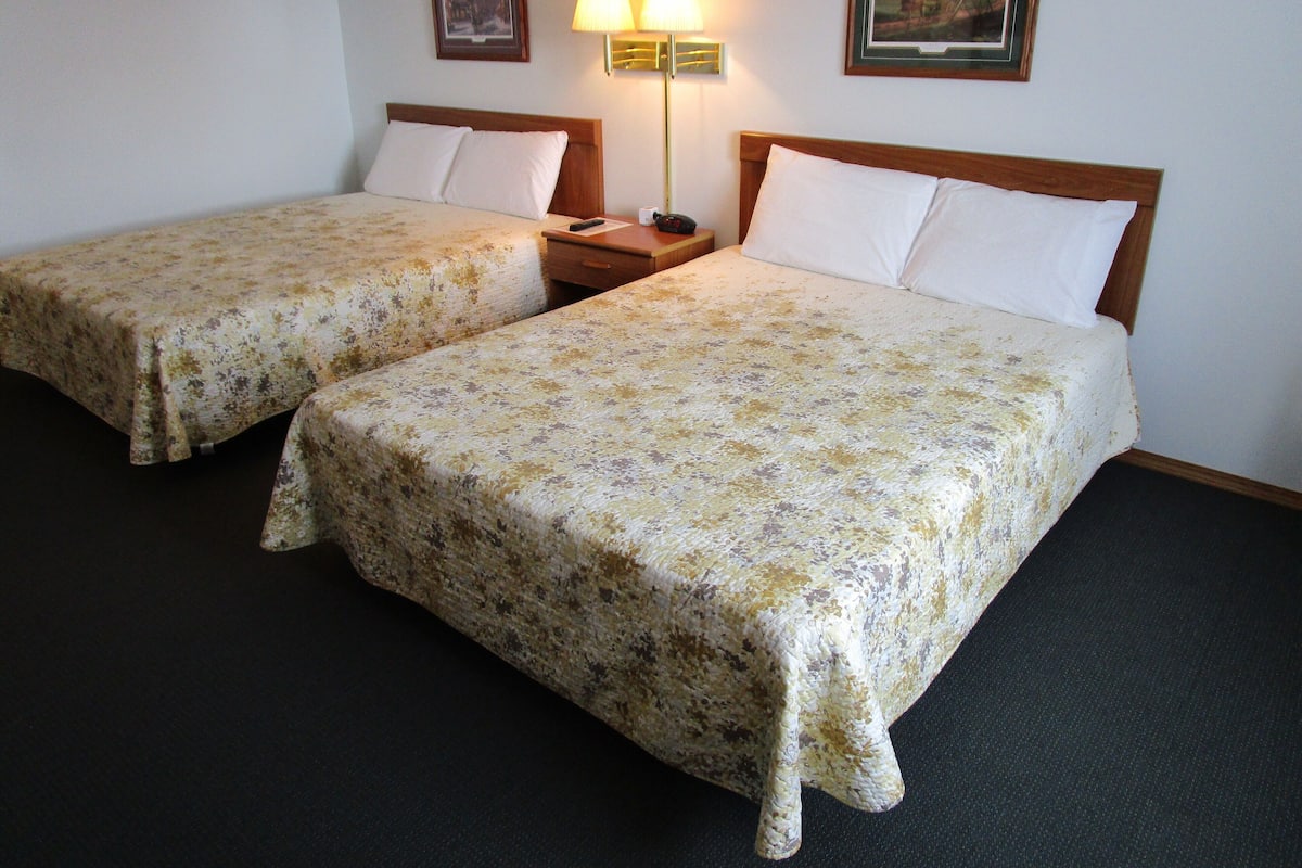 Two single beds with floral bedspreads, a nightstand with a lamp, and two framed pictures on the wall.