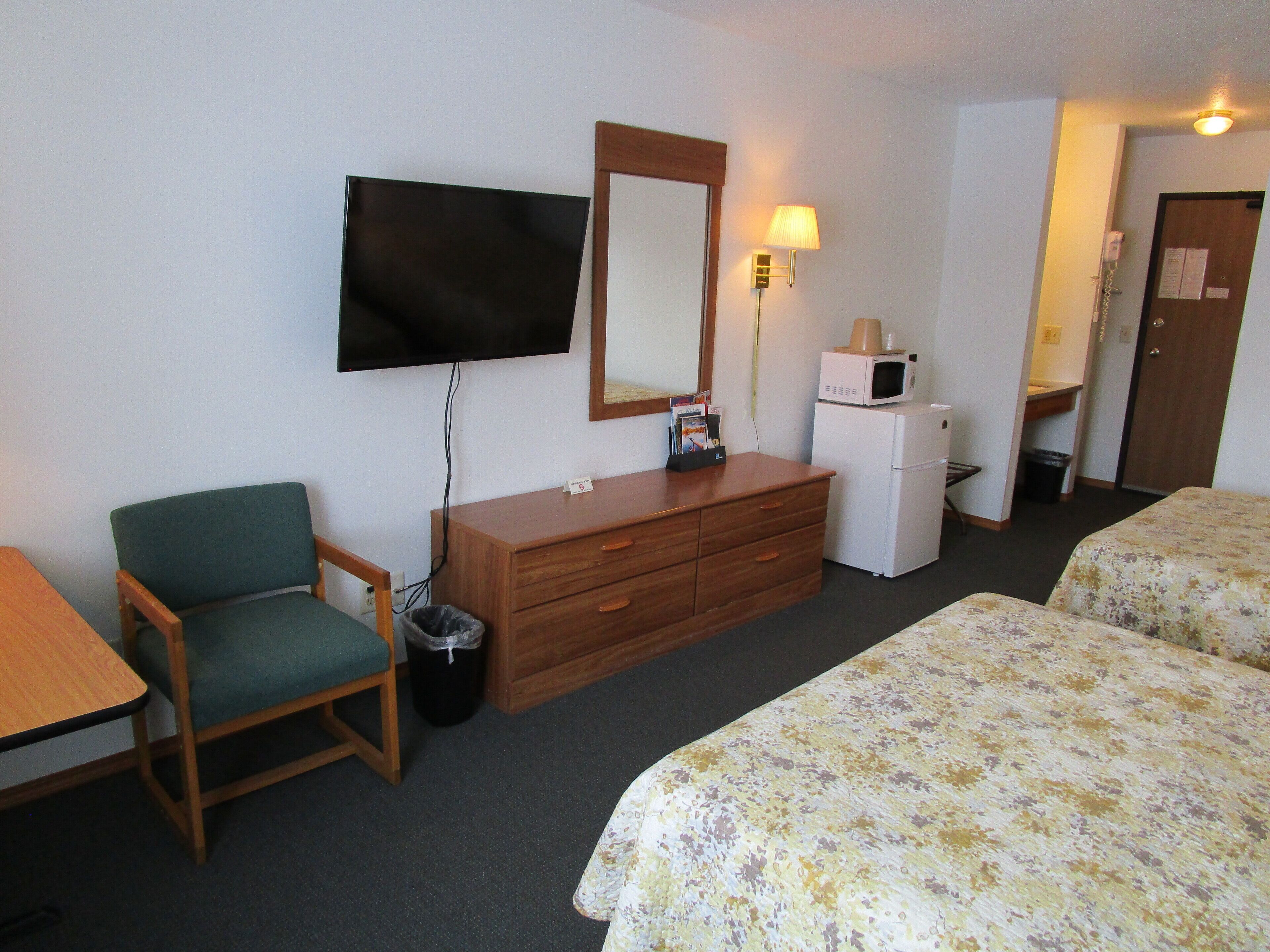 Ein Hotelzimmer mit Fernseher, einer Holzkombie, einer Mikrowelle, einem Mülleimer, einem grünen Sessel und zwei Betten mit Blumenmuster-Bettwäsche.
