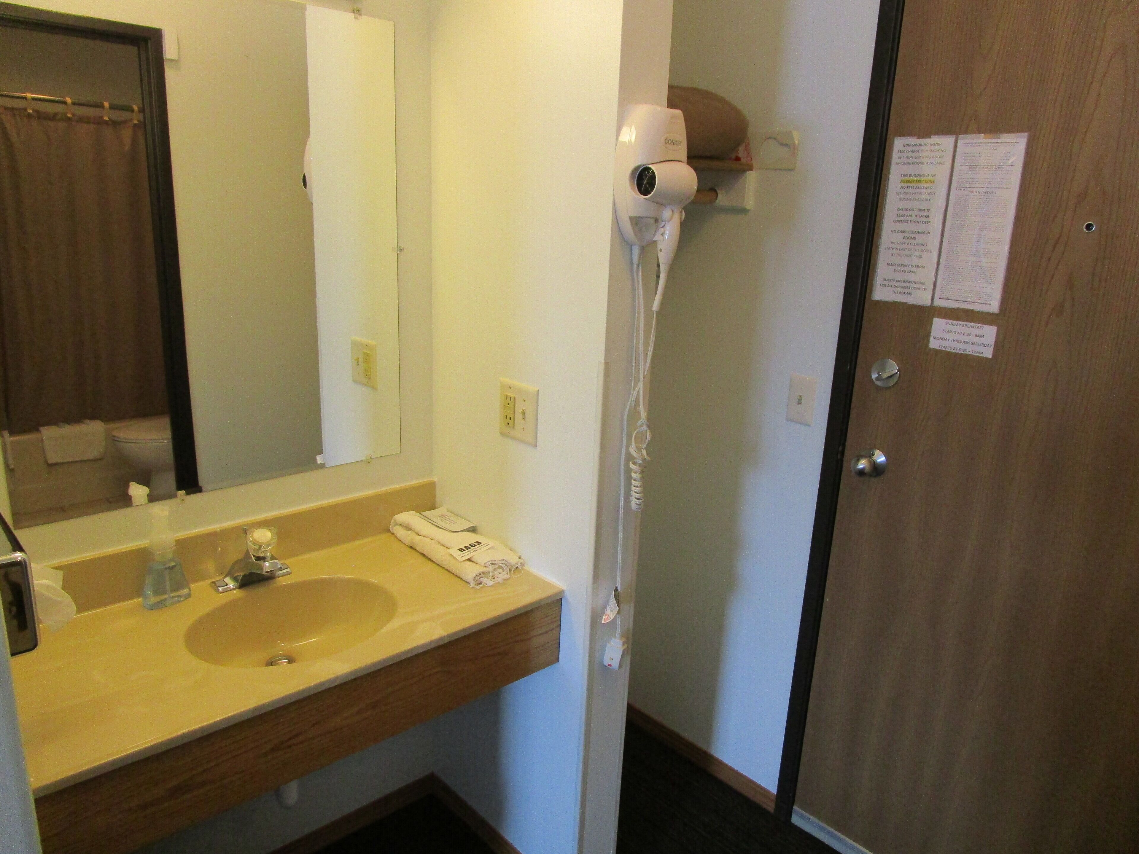 Une salle de bain équipée d’un lavabo, d’un miroir, d’un sèche-cheveux et d’une porte avec une pancarte.