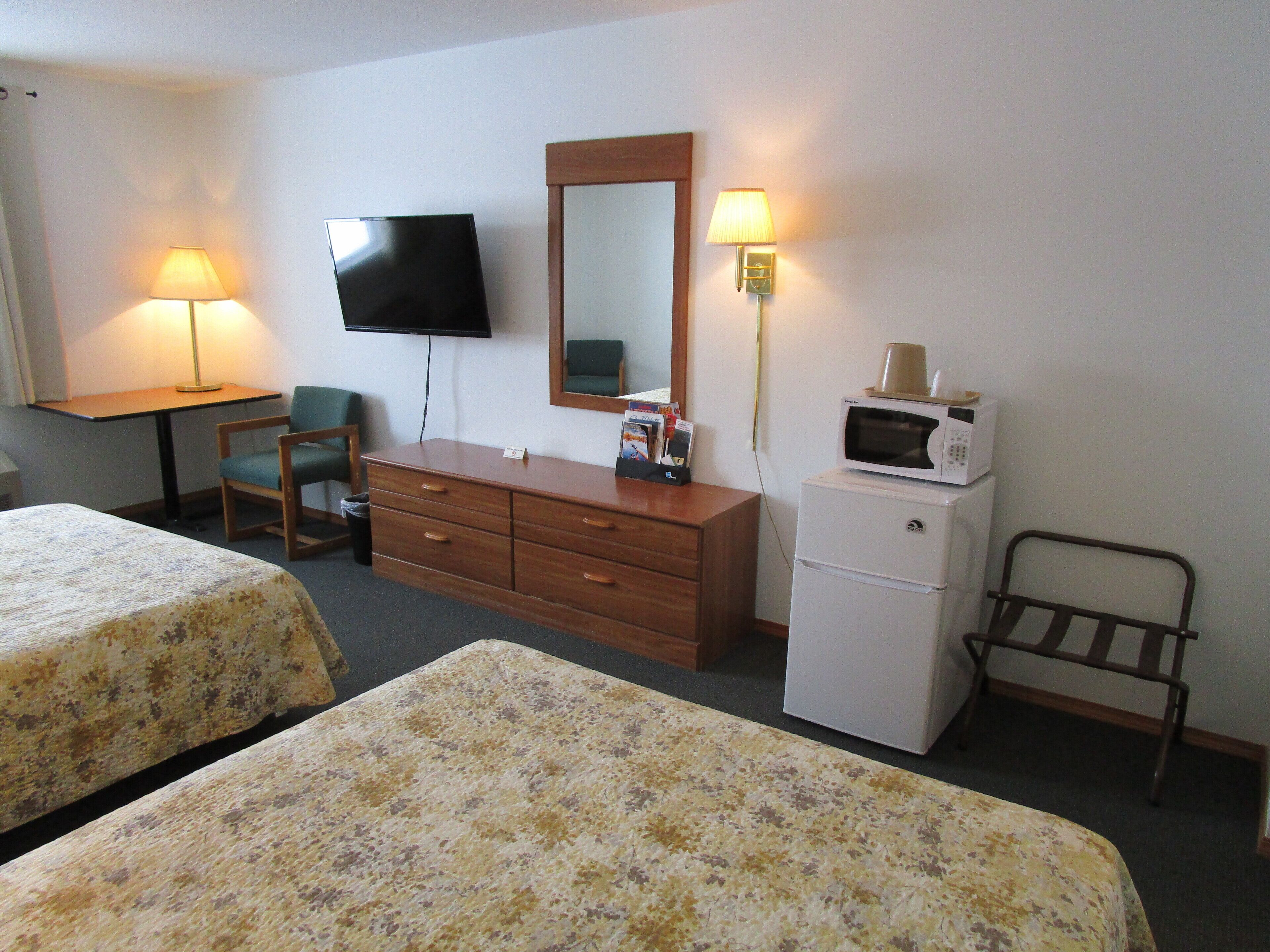 Quarto de hotel com duas camas, uma escrivaninha, televisão, cômoda, micro-ondas e duas luminárias.
