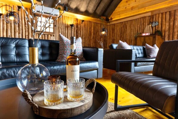 A cozy room with leather sofas, a wooden wall, and a tray with glasses and a bottle. - North Star Beach Suites (Louisbourg)