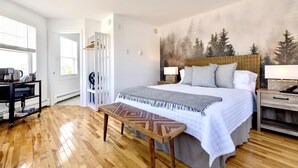 Un dormitorio con cama, mesitas de noche, un banco, un armario y un mural en la pared.