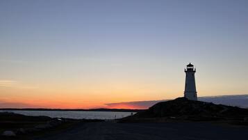 A lighthouse on a rocky outcrop with a clear sky and a sunset in the background.