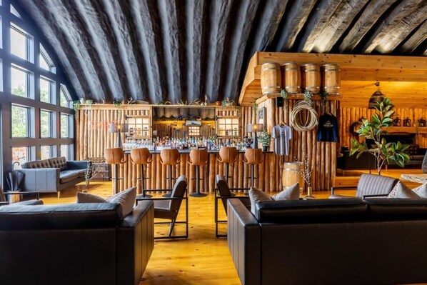A rustic interior with wooden beams, a bar area with stools, and leather seating.
