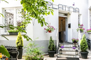 A hotel entrance with a white facade, potted plants, and outdoor seating. - Platinia Apartments (Kraków)