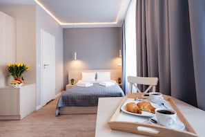 A modern hotel room with a neatly made bed, a breakfast tray with croissants and coffee, and a vase of flowers on the side table. - Platinia Apartments (Kraków)