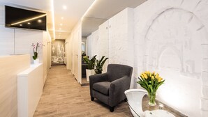 A modern reception area with a grey armchair, a white reception desk, and a wall with a stone-like texture. - Platinia Apartments (Kraków)