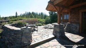 A stone patio with outdoor furniture, a wooden cabin structure, and a natural landscape with trees and rocks. - Glacier Luxury Lodge (Truckee)