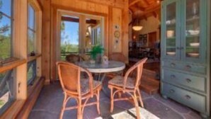 A wooden cabin interior with a round table and two chairs, a cabinet with glass doors, and a view of the outdoors. - Glacier Luxury Lodge (Truckee)