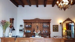 Ein hölzerner Empfangstresen mit einer großen Bücherwand dahinter, eine Chandelier darüber und ein Spiegel an der Wand.