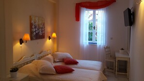 A bedroom with two beds, a desk, a TV, and a window with curtains. - Ippokampos Hotel (Hydra)