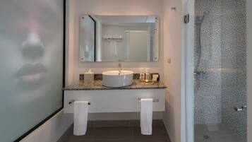A modern bathroom with a granite countertop, a round sink, a large mirror, and a shower with a perforated glass door.