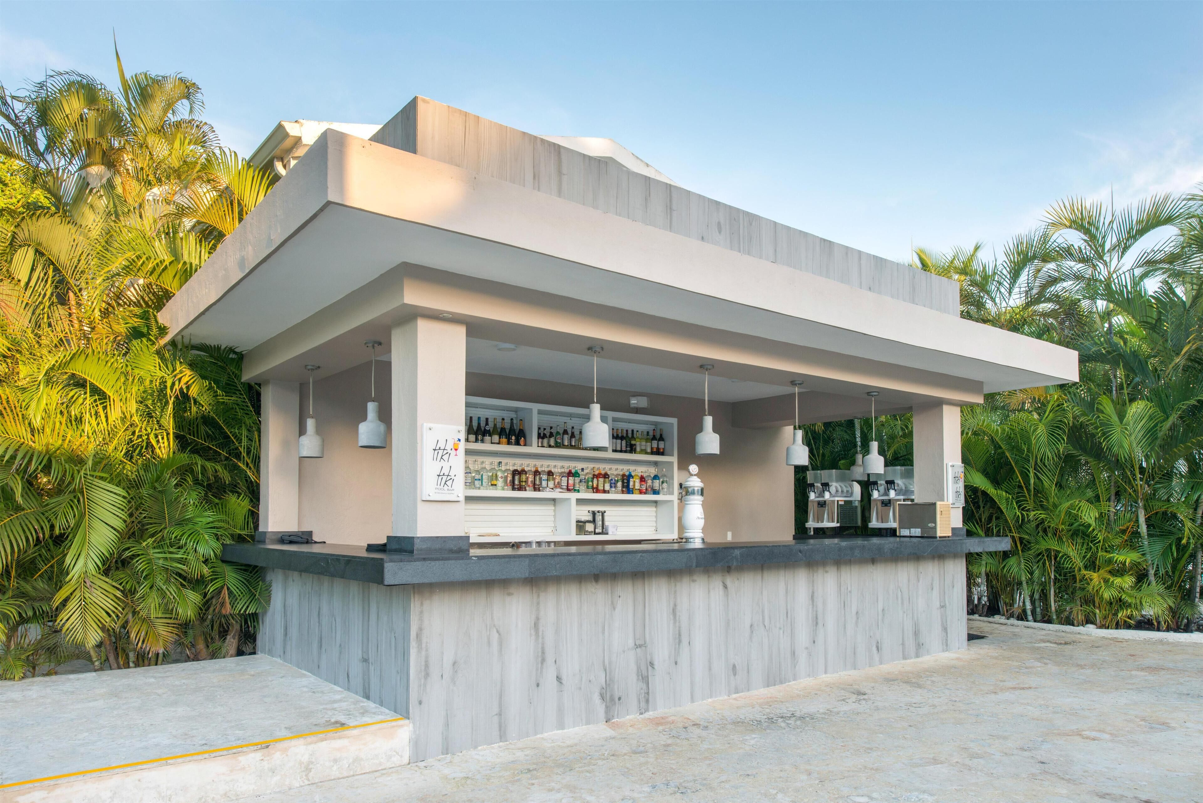 A modern outdoor bar with a concrete counter, hanging pendant lights, and a variety of bottles.