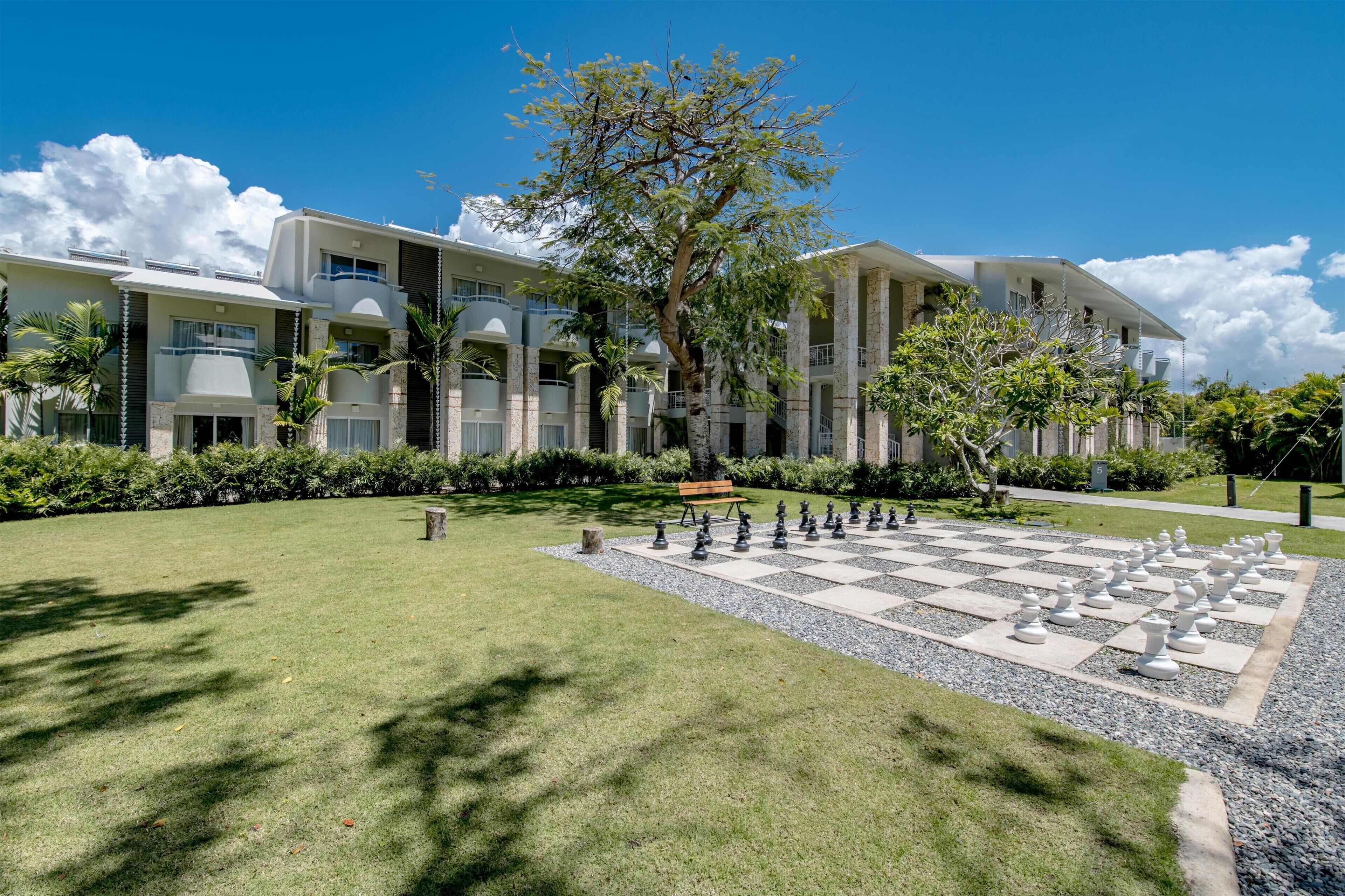 A modern hotel with a spacious courtyard featuring a large chessboard and a bench.