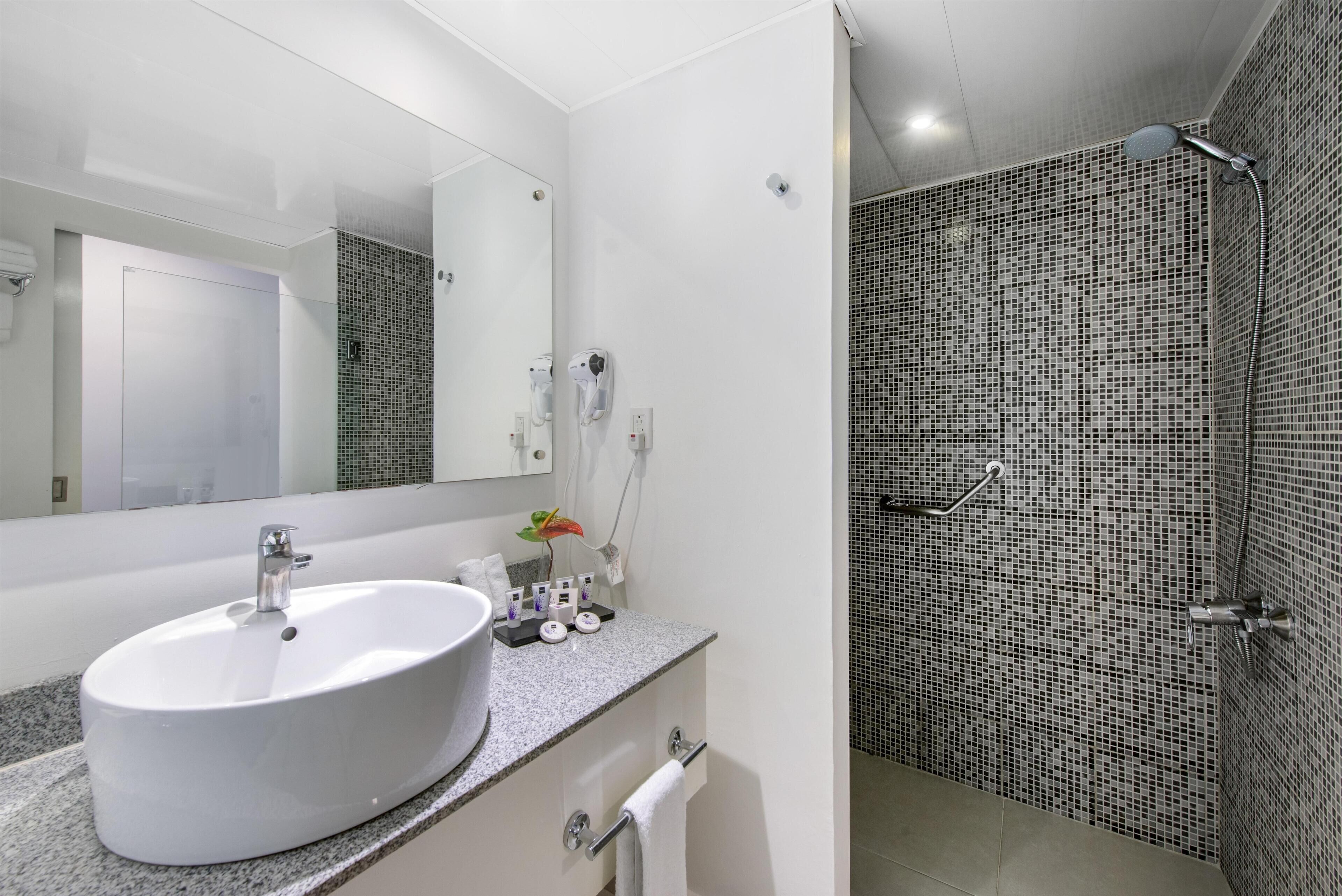 A modern bathroom with a large white sink, a mirror, and a shower with mosaic tiles.