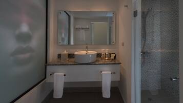 A modern bathroom with a granite countertop, a white sink, a large mirror, and a shower with a perforated glass door.