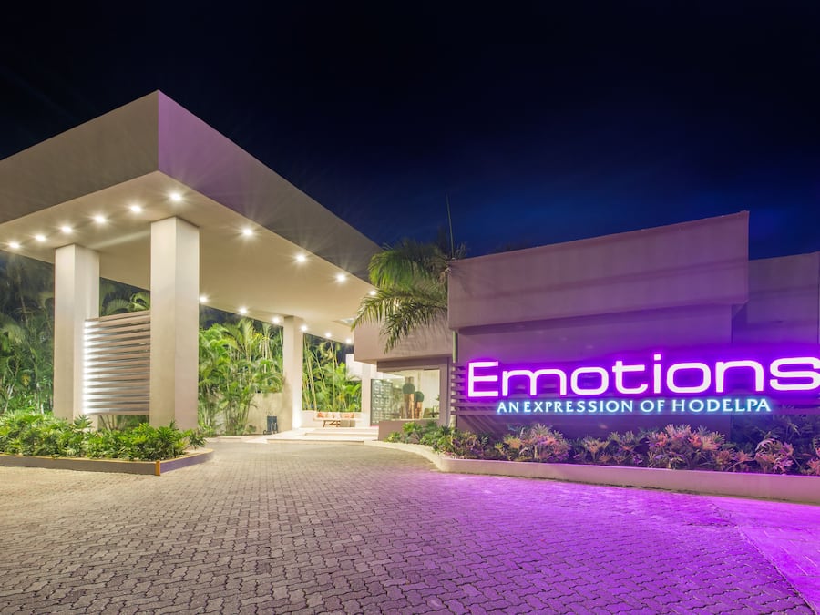Een moderne hotelentree met een neonbord waarop staat: "Emotions AN EXPRESSION OF HODELPA" en een geplaveid pad dat naar de ingang leidt.