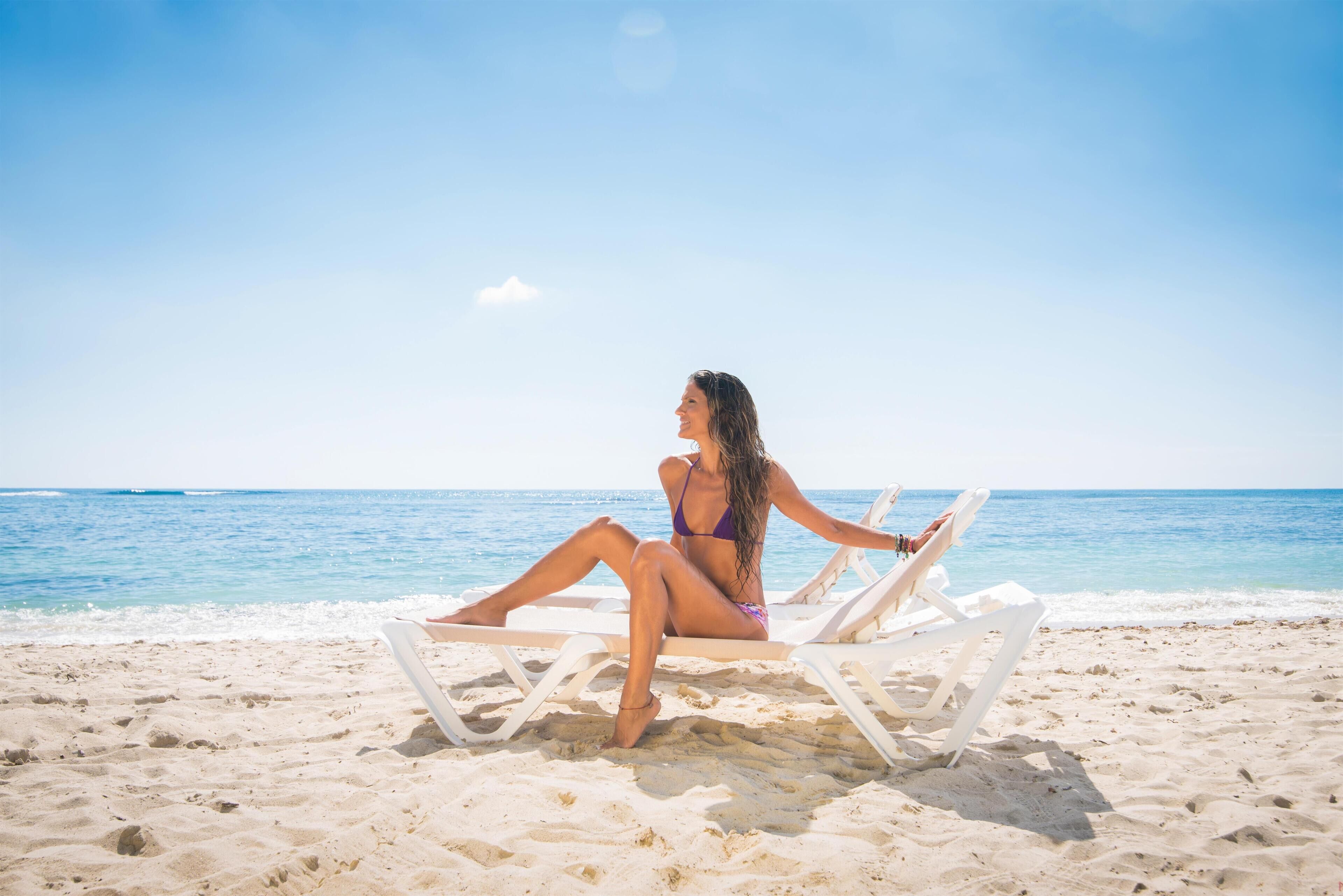A woman sitting on a beach chair facing the ocean.