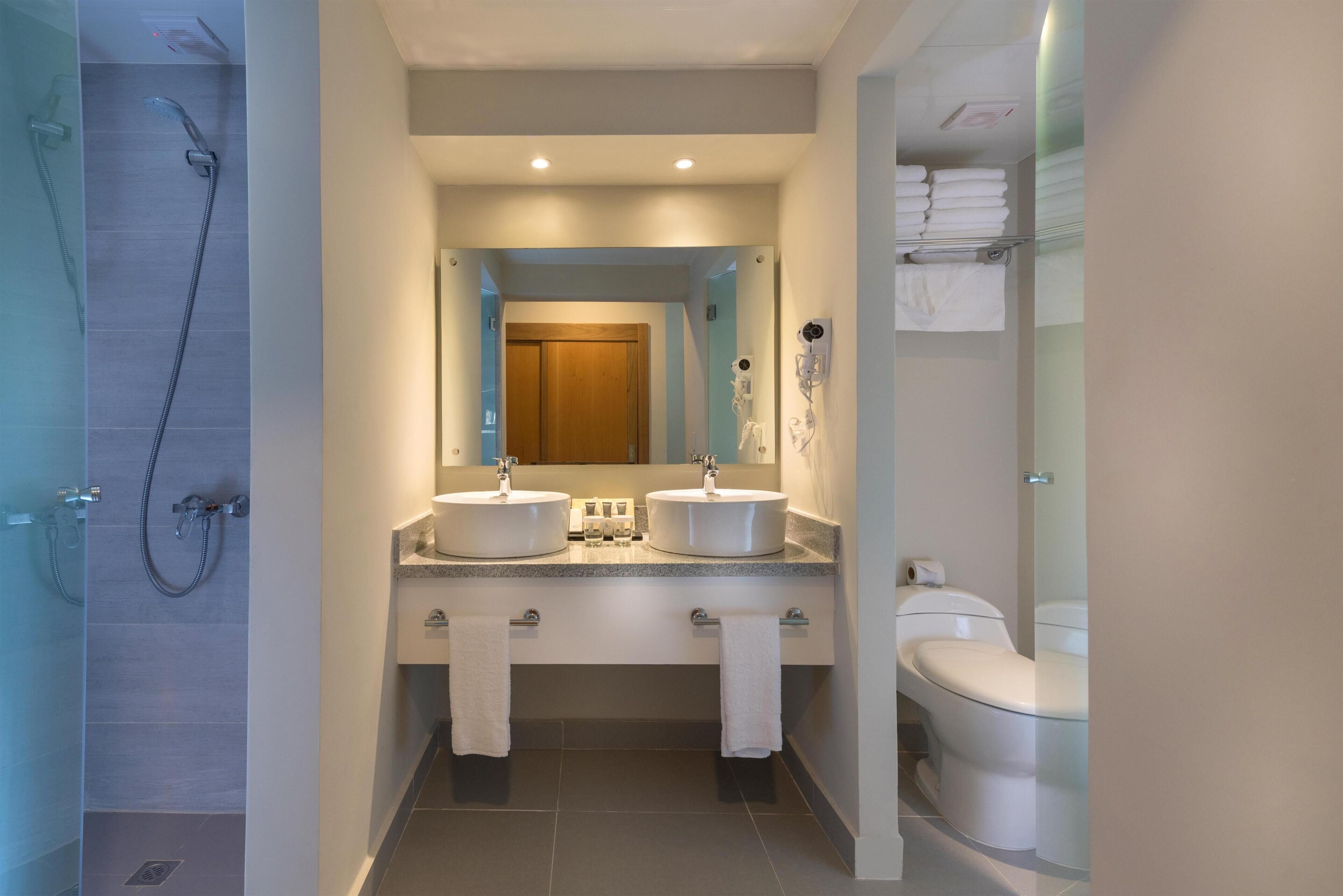 A modern bathroom with a glass shower enclosure, two sinks with mirrors, a toilet, and a towel rack.
