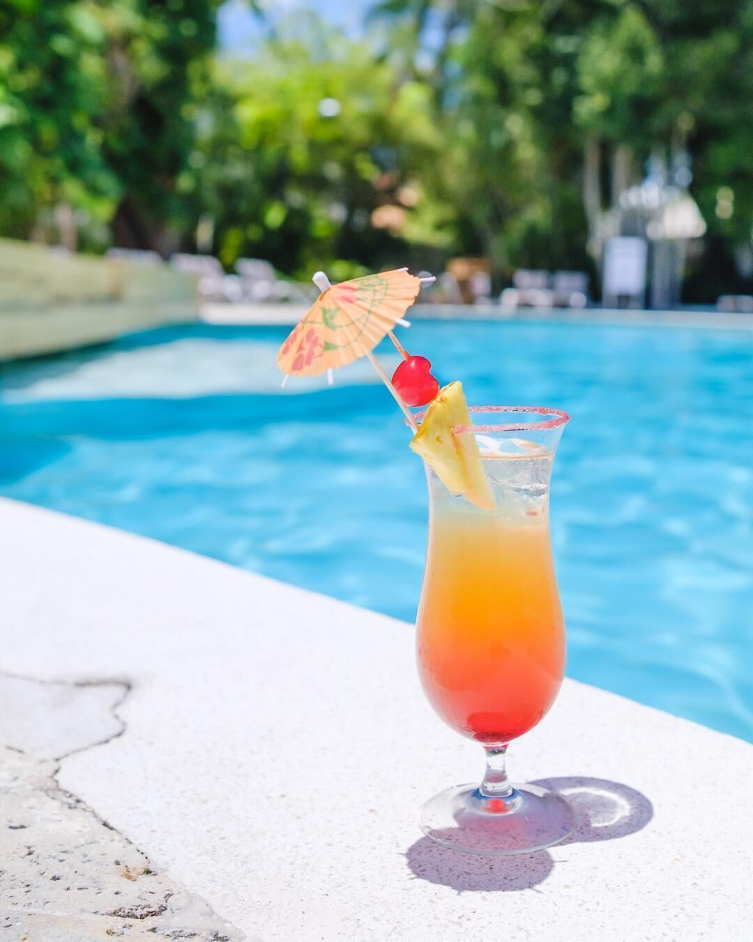 A cocktail with a tropical umbrella and fruit garnish by a poolside.