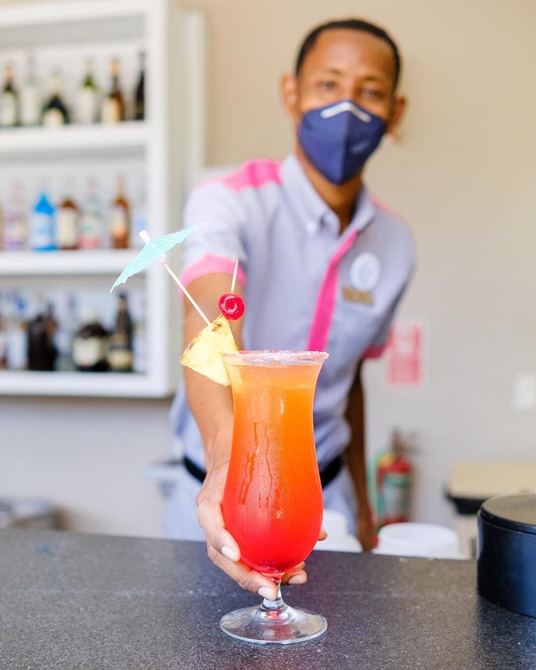 Ein Barkeeper hält einen Cocktail mit Ananas-Garnitur und Trinkhalm.
