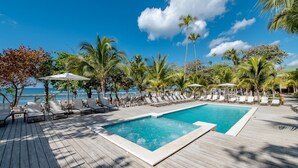 A poolside area with lounge chairs and umbrellas, surrounded by palm trees and a view of the ocean.