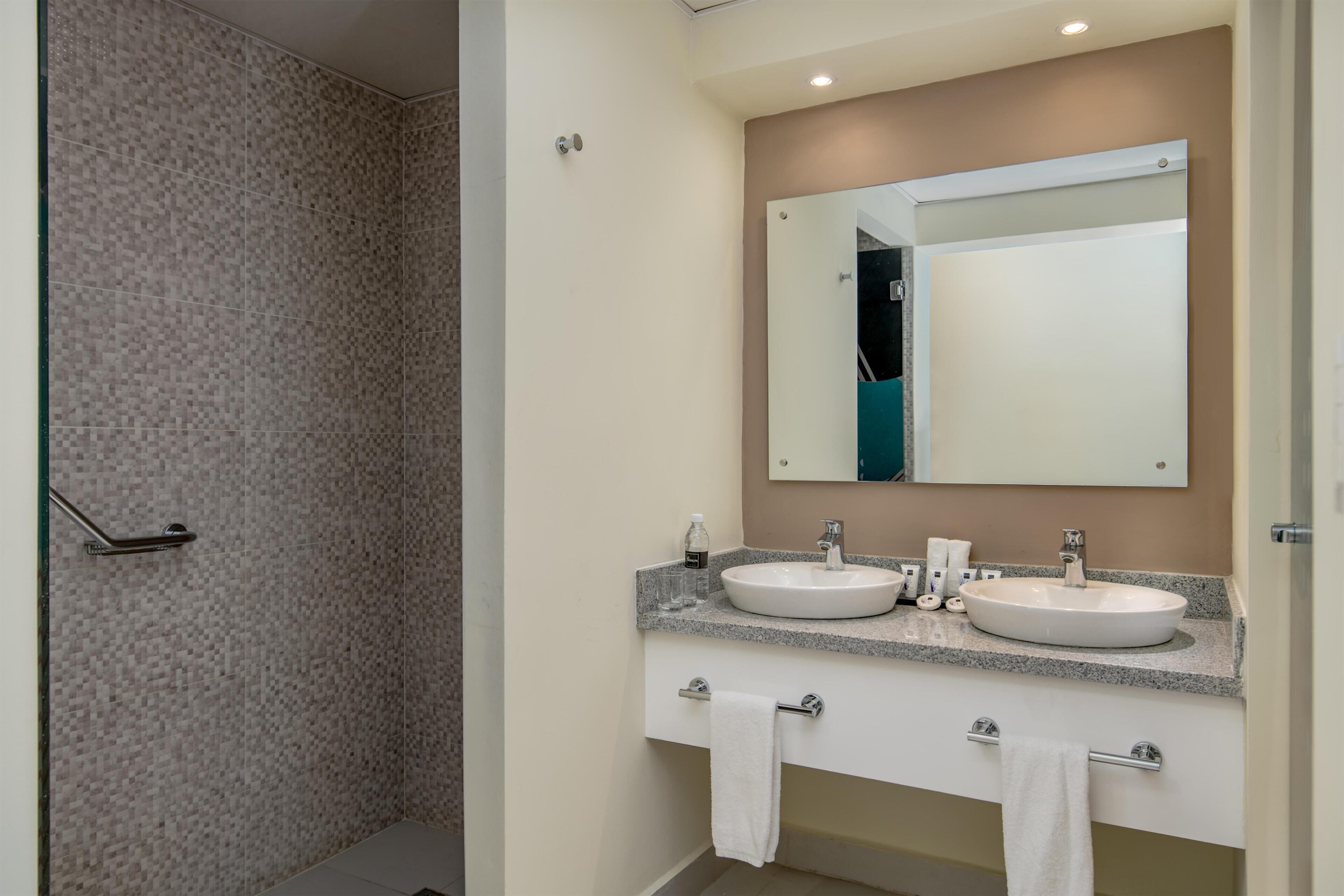 A modern bathroom with two sinks, a large mirror, and a shower area.