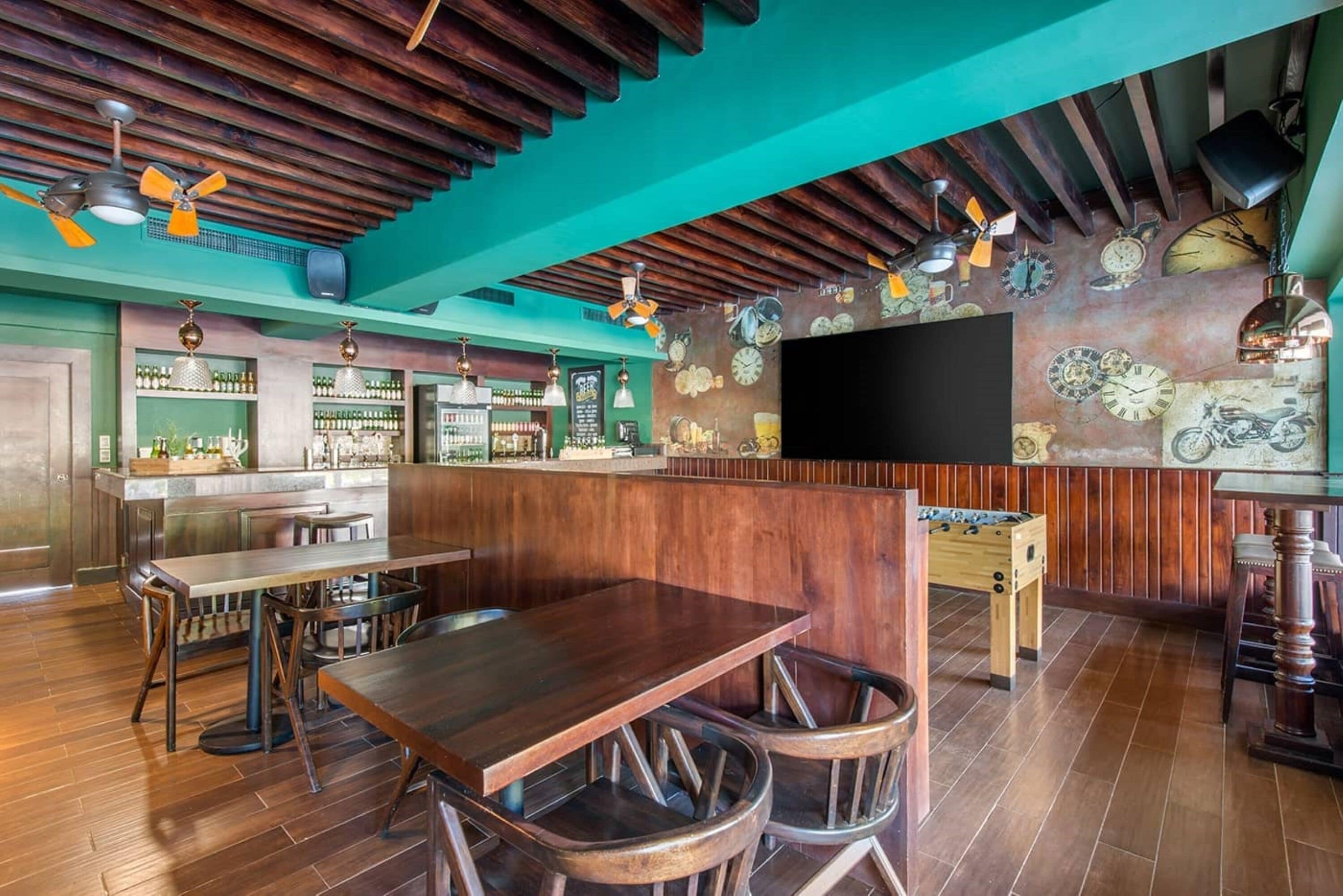 Angolo bar con arredi in legno, un'ampia televisione a schermo piatto e una parete decorata con orologi e oggetti vintage.