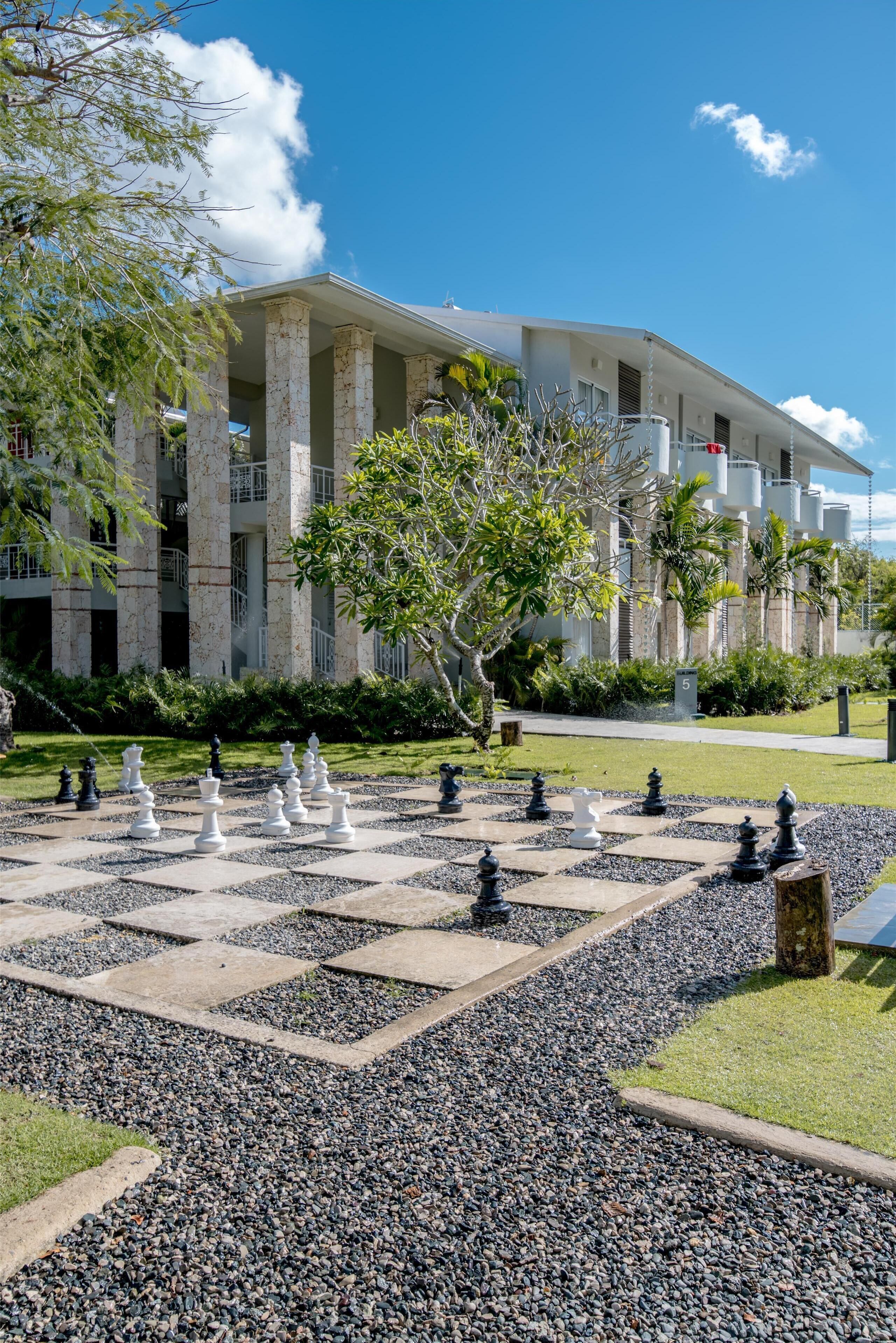 A courtyard with a chessboard, palm trees, and a building with columns and balconies.