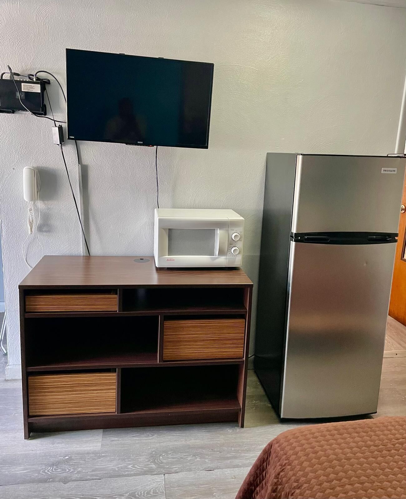 A compact kitchenette with a microwave, a refrigerator, and a flat-screen TV mounted on the wall.