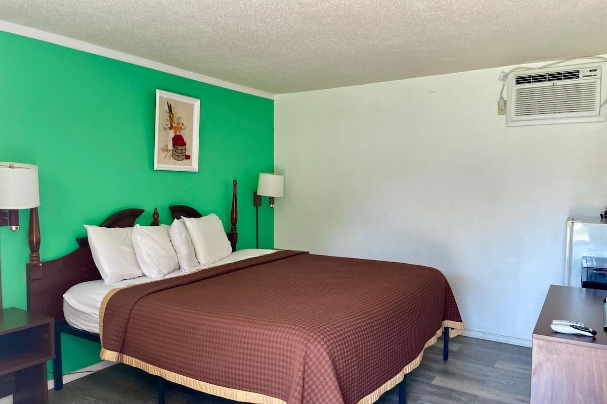 A room with a bed, two bedside tables, a wall-mounted air conditioner, and a framed picture.