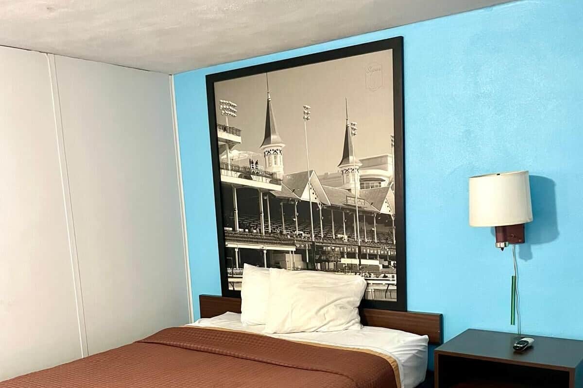 A hotel room with a bed, a nightstand, a lamp, and a large framed picture of a building.